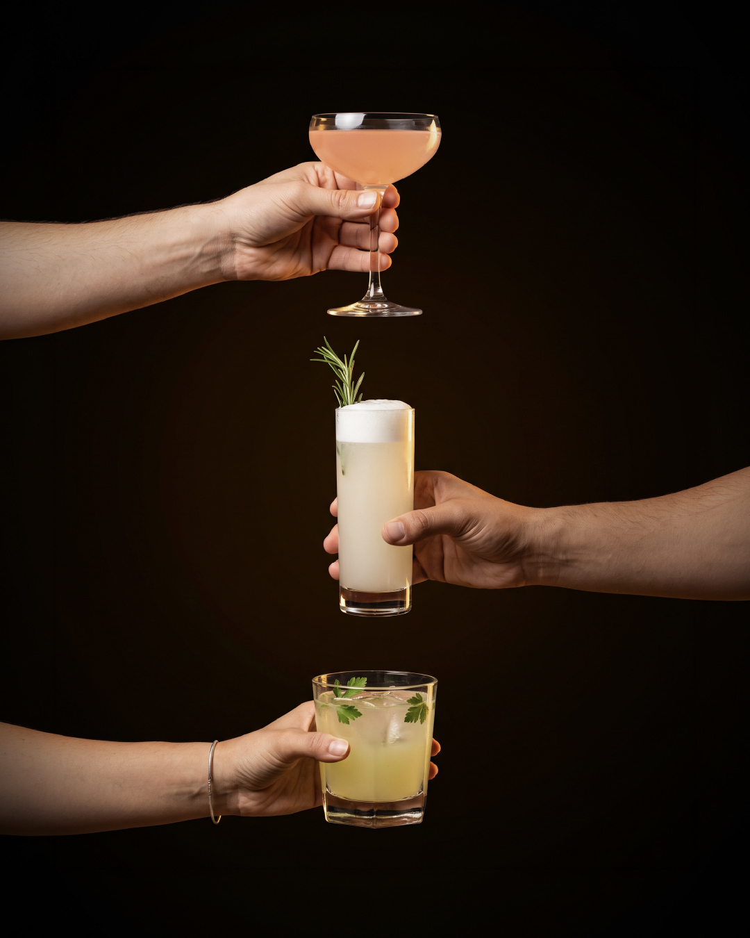 Three hands holding the three winning cocktails from the Batch 22 Cocktail Contest: Pianosa in a coupe, Buzz Fizz in a tall glass and Herb Garden in a rocks glass